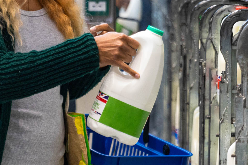 Mid-adult woman shopping on a budget. She is looking for low prices due to inflation, standing and holding a milk carton. She is living in the North East of England.
